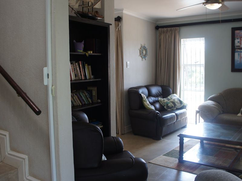A comfortable living room area featuring a staircase with a wooden handrail, a ceiling fan, and access to a window with a security gate.