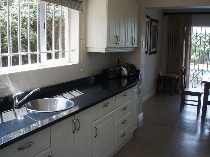 A functional kitchen featuring granite countertops, white cabinetry, and a stainless steel sink, with an adjacent dining area visible through the doorway.