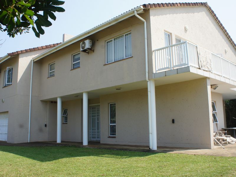 Rear view of a two-story townhouse featuring a covered patio, upper-level balcony, and integrated garage with a well-maintained lawn.