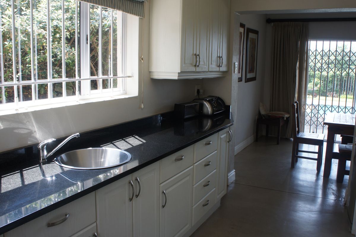 A functional kitchen featuring granite countertops, white cabinetry, and a stainless steel sink, with an adjacent dining area visible through the doorway.