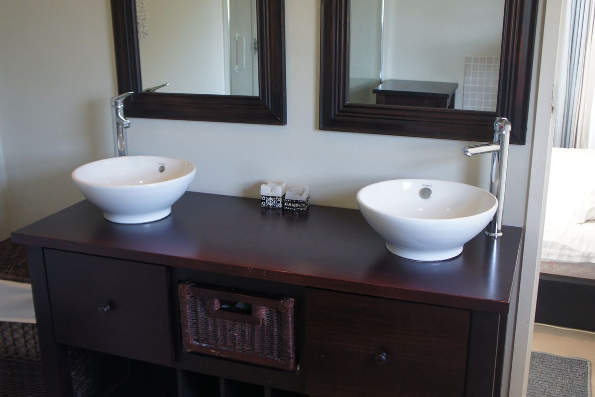 A well-maintained bathroom featuring a dark wood double vanity with dual vessel sinks, chrome mixer taps, and matching framed wall mirrors.