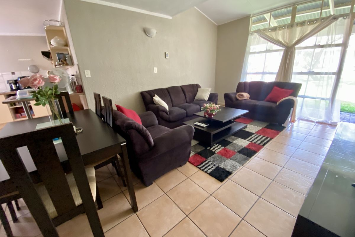 Open-plan living and dining area featuring tiled flooring, vaulted ceilings, and large windows providing natural light, with an adjacent kitchen space.