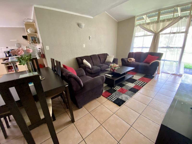 Open-plan living and dining area featuring tiled flooring, vaulted ceilings, and large windows providing natural light, with an adjacent kitchen space.