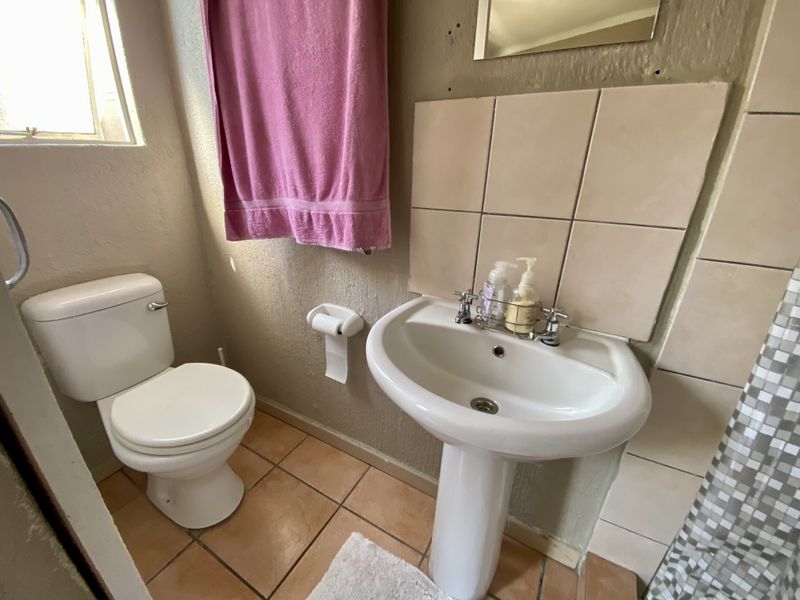 Compact bathroom featuring a pedestal basin, ceramic toilet, and tiled splashback, requiring cosmetic updates to improve the overall finish.