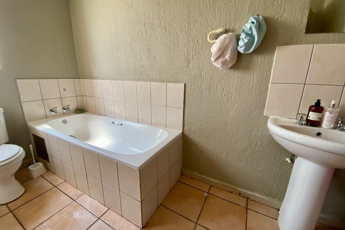 A dated bathroom featuring a built-in bathtub, pedestal basin, and ceramic floor tiles, requiring cosmetic updates to improve its overall condition and appeal.