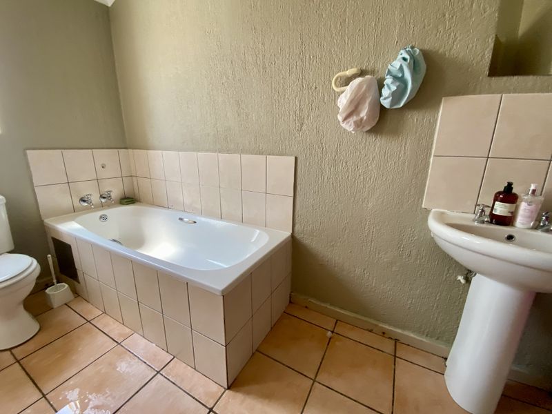 A dated bathroom featuring a built-in bathtub, pedestal basin, and ceramic floor tiles, requiring cosmetic updates to improve its overall condition and appeal.
