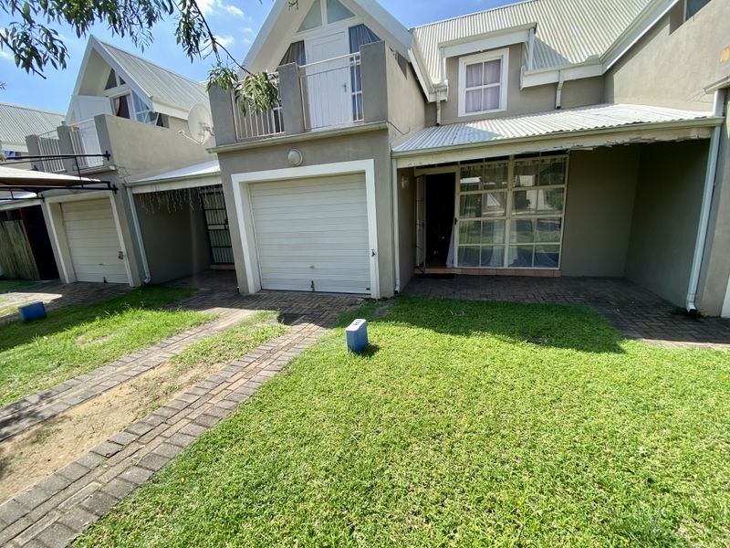 Front exterior view of a residential apartment unit featuring a single garage, upper-level balcony, and a small private lawn area.