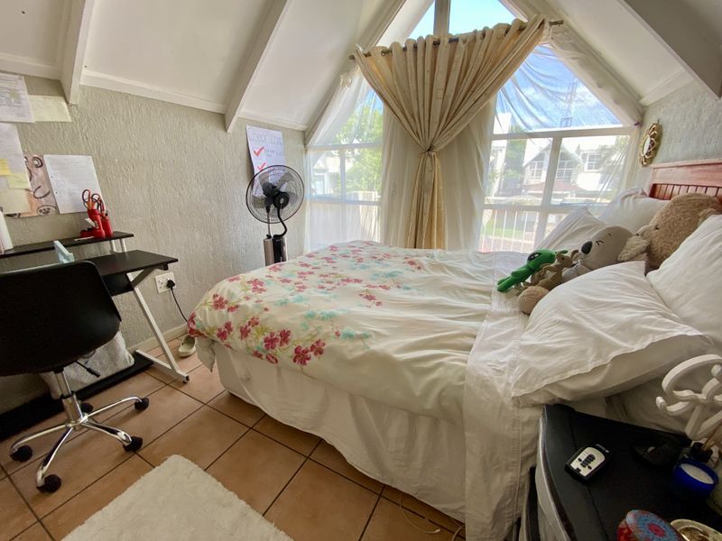 A bedroom featuring a pitched ceiling, tiled flooring, and a large triangular window that provides natural light.
