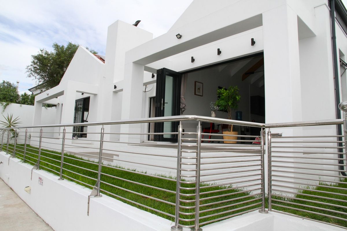 Modern rear exterior view featuring a raised patio, stainless steel balustrades, and large bi-fold doors leading into the living area.
