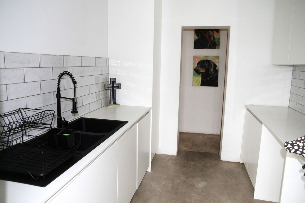 A modern galley-style kitchen featuring white cabinetry, stone countertops, a black double sink with a gooseneck faucet, and subway tile backsplash.