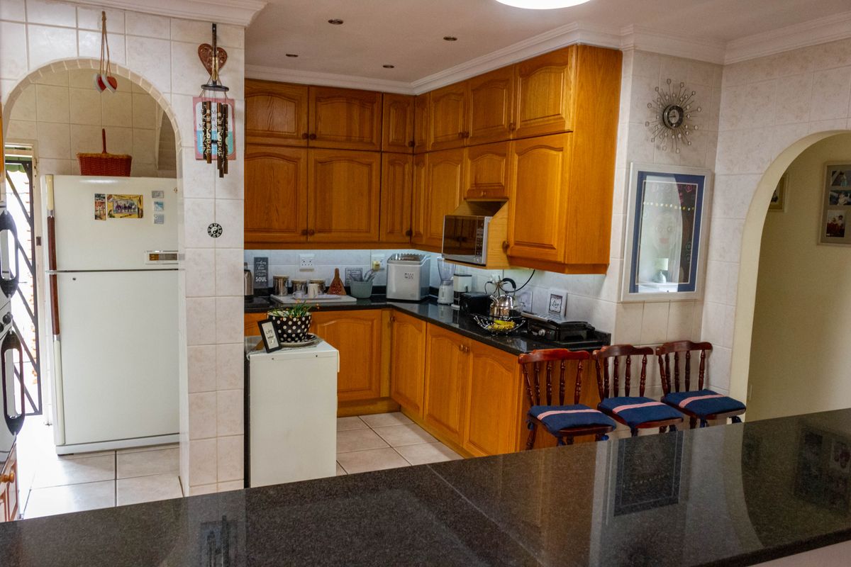 A functional kitchen featuring warm wooden cabinetry, granite countertops, and a tiled backsplash, connected to adjacent living spaces via an open archway design.