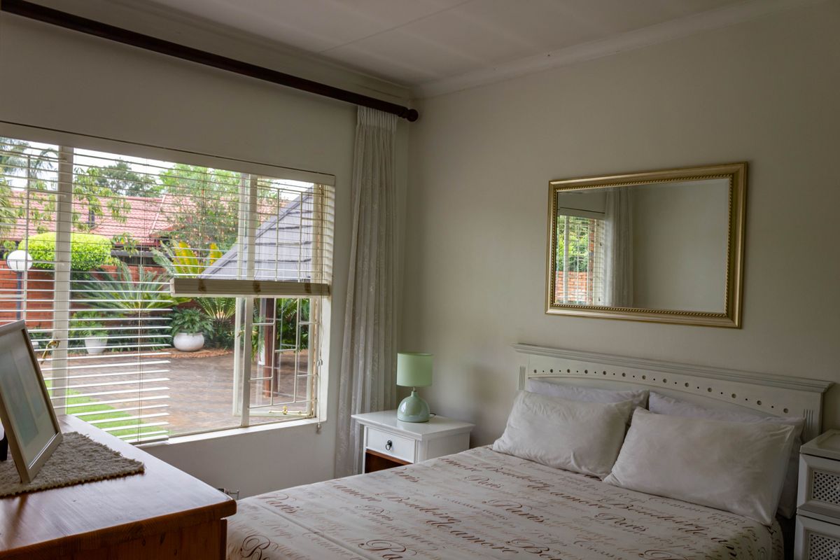 A well-lit bedroom featuring a large window with garden views, neutral wall finishes, and a built-in headboard.
