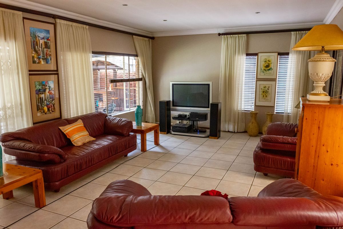 Spacious living room featuring neutral tiled flooring, recessed downlighting, and large windows with venetian blinds and curtain rails.