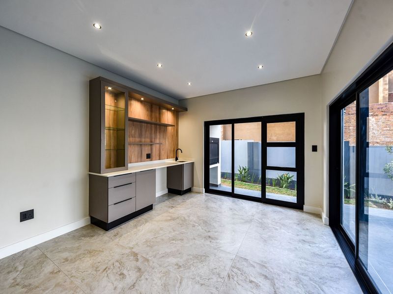 Modern scullery or bar area featuring built-in cabinetry, stone countertop, integrated sink, and large sliding glass doors opening to an outdoor space.