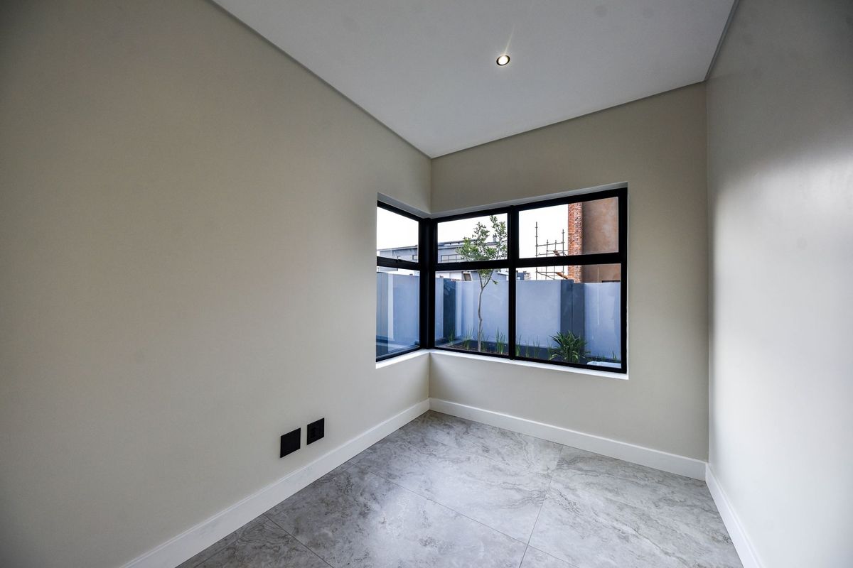 A bright, modern, empty room featuring large corner windows with black frames, neutral walls, and contemporary grey tiled flooring.