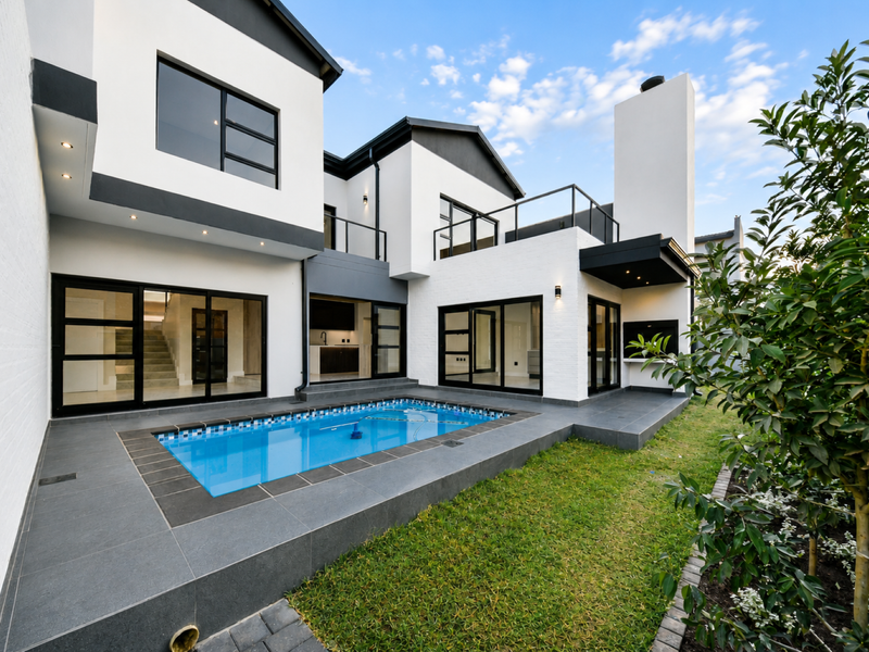 Modern rear exterior featuring a swimming pool, tiled patio, built-in braai, and contemporary architectural design with large glass sliding doors.