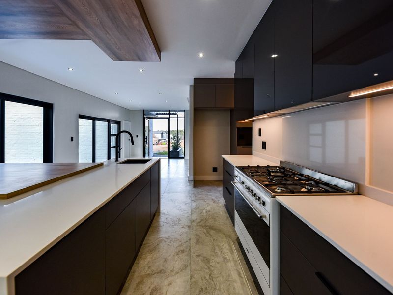 Modern kitchen featuring dark cabinetry, stone countertops, a large central island, and a high-end gas range, seamlessly flowing into the open-plan living area.