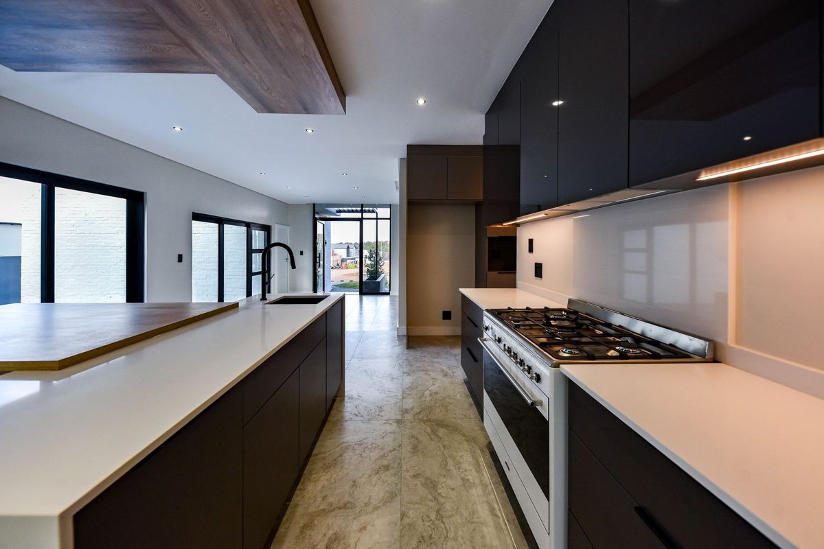 Modern kitchen featuring dark cabinetry, stone countertops, a large central island, and a high-end gas range, seamlessly flowing into the open-plan living area.