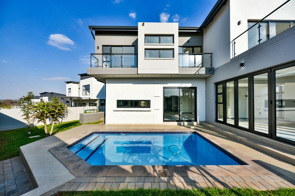 Modern rear exterior view featuring a swimming pool, paved patio area, and a contemporary two-story building with glass balconies.