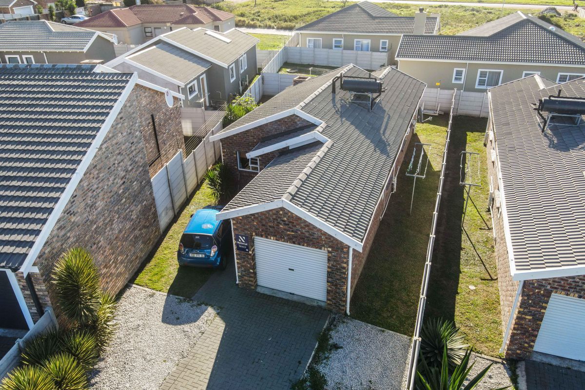 Aerial view of a residential property featuring a brick facade, tiled roof with solar water heater, paved driveway, and a secure garage.
