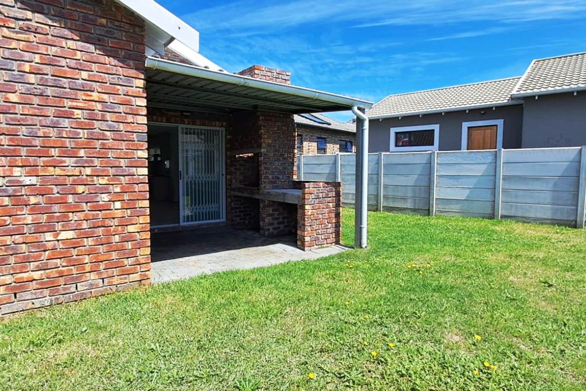 Rear view of the property featuring a brick facade, a covered patio with a built-in braai, and a private garden with precast walling.