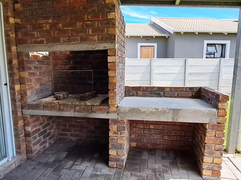 Covered patio area featuring a built-in brick braai with concrete prep space, overlooking a private garden with precast boundary walling.