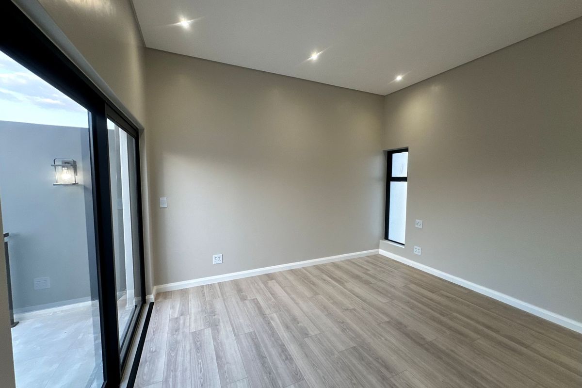 A bright, modern, and empty bedroom featuring neutral walls, wood-look flooring, recessed ceiling lighting, and large sliding glass doors leading to an outdoor area.