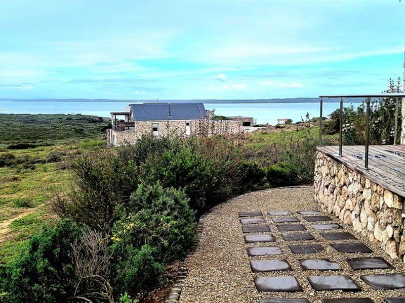 A scenic view from a stone-clad patio featuring a timber deck, stainless steel balustrade, and stone paving, overlooking a coastal landscape.