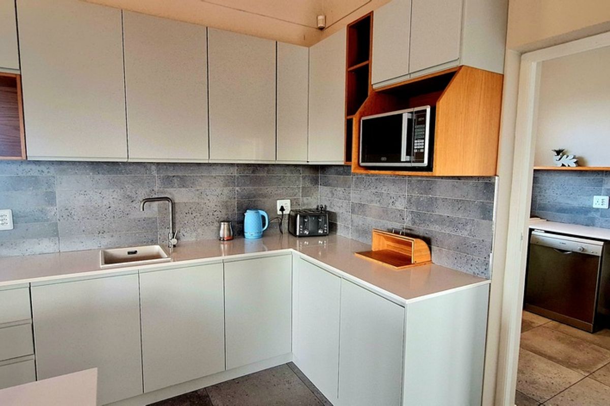 Modern kitchen featuring light grey cabinetry, stone countertops, grey tiled backsplash, and an adjacent scullery area with additional workspace and plumbing.