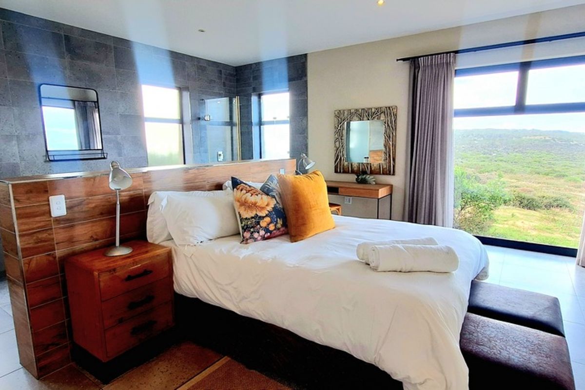 Spacious bedroom featuring a modern open-plan layout with a built-in headboard partition, tiled flooring, and large windows offering scenic natural views.