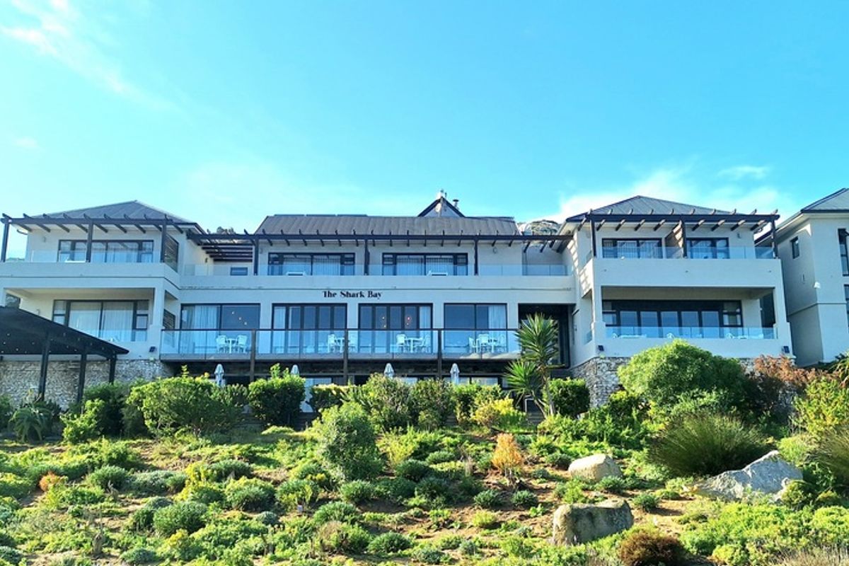 A rear view of a multi-level coastal property featuring expansive balconies, glass balustrades, and landscaped terraced gardens.