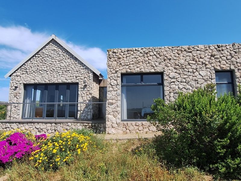 A modern stone-clad exterior featuring large aluminium windows and sliding doors, opening onto a raised deck area with natural garden surroundings.