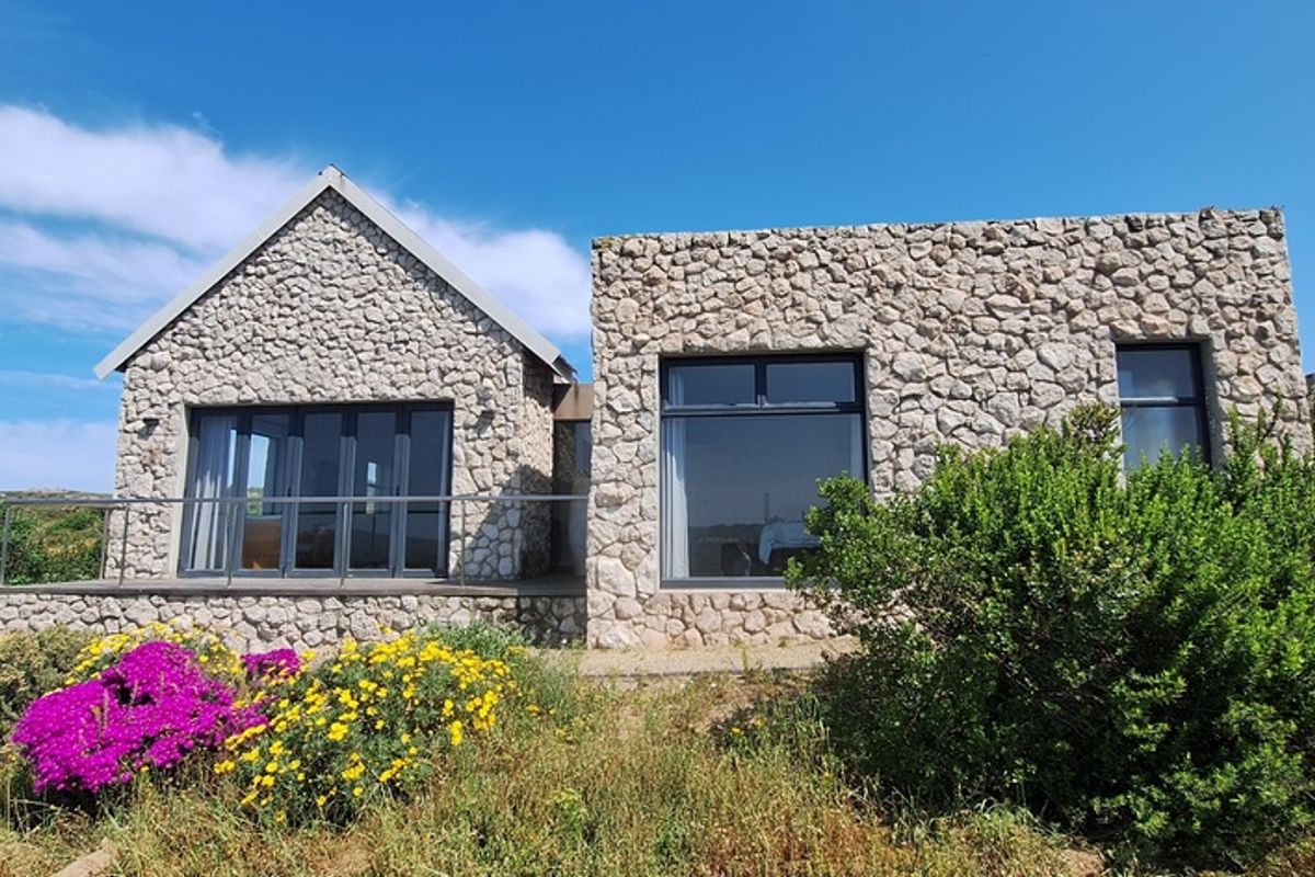 A modern stone-clad exterior featuring large aluminium windows and sliding doors, opening onto a raised deck area with natural garden surroundings.
