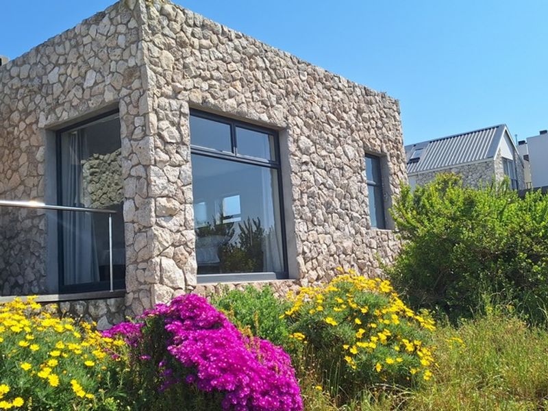 A modern residential exterior featuring natural stone cladding, large aluminium-framed windows, and a stainless steel balustrade overlooking a landscaped garden area.