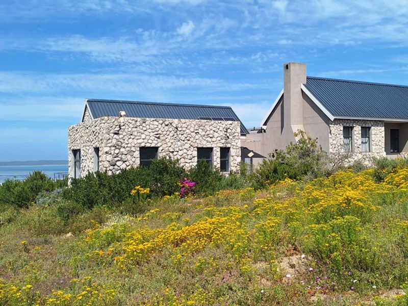 A scenic view of the rear elevation featuring stone-clad walls, a modern metal roof, and a chimney, set against a natural coastal landscape.
