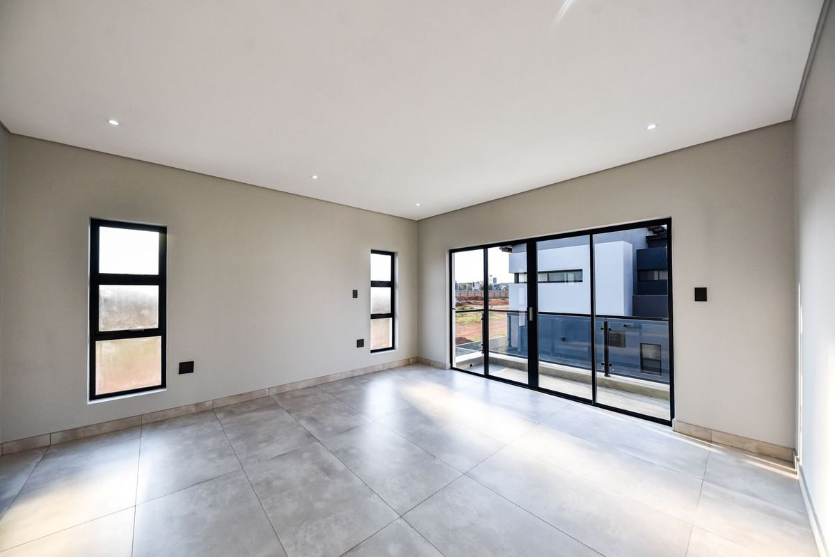 A bright, modern, and empty living room featuring large format floor tiles, recessed downlights, and sliding glass doors leading to a balcony.
