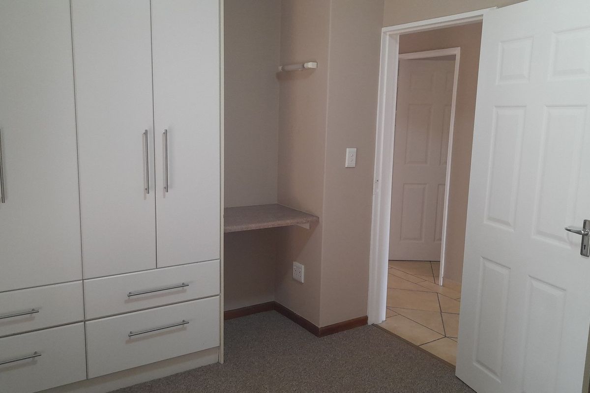A bedroom featuring built-in white cabinetry with integrated drawers and a small built-in desk area, leading into a tiled hallway.