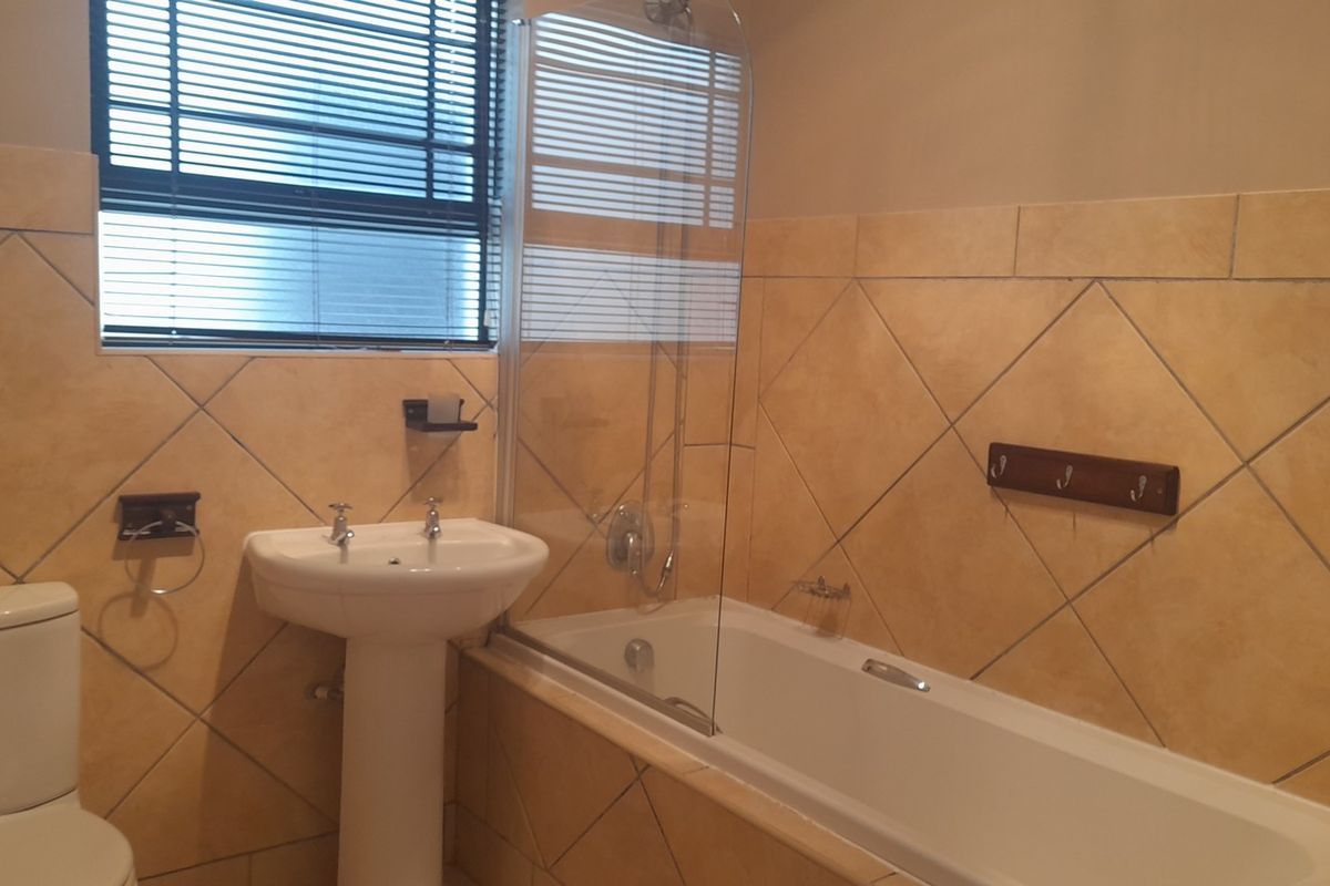 A functional bathroom featuring a pedestal basin, a bathtub with a glass shower screen, and diamond-patterned wall tiles.