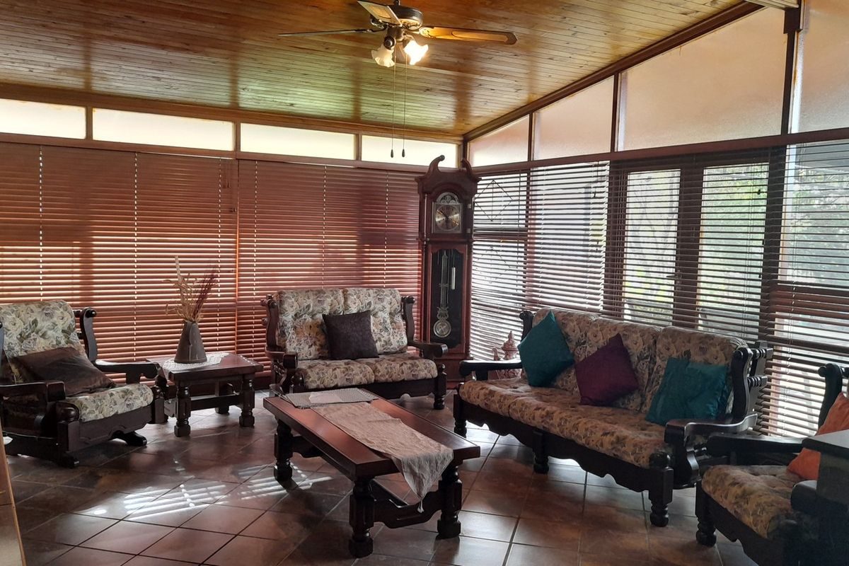 Spacious living area featuring a warm timber-clad ceiling, ceiling fan, and tiled flooring, surrounded by large windows with venetian blinds for natural light.
