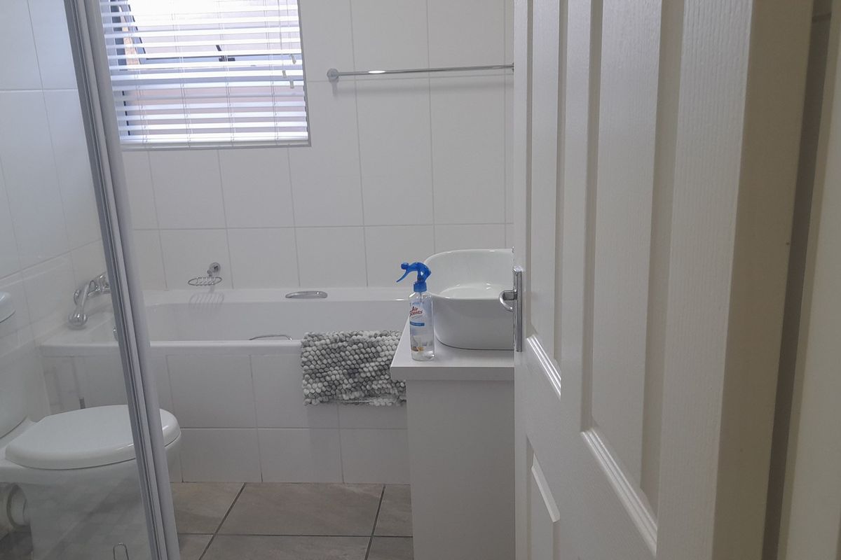 A functional bathroom featuring a white bathtub, a modern vessel sink on a vanity, a toilet, and tiled walls and flooring.