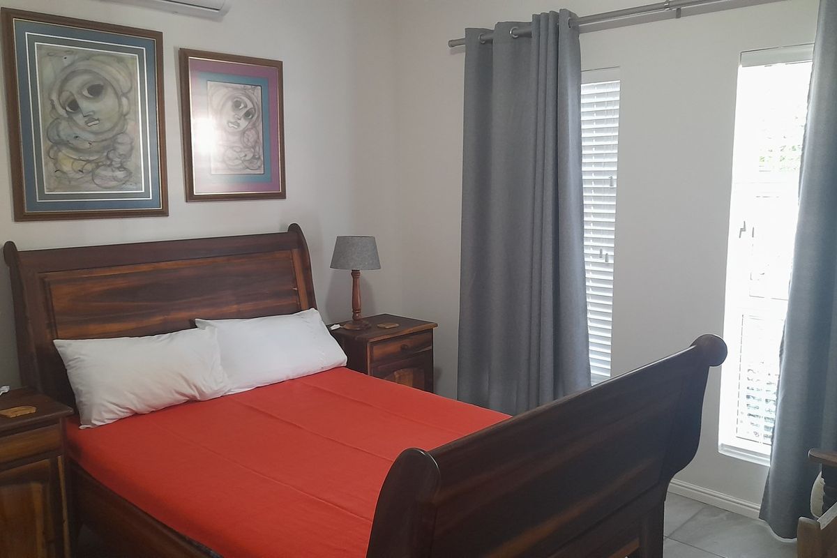 A well-lit bedroom featuring tiled flooring, a wall-mounted air conditioning unit, and large windows with fitted curtain tracks and blinds.