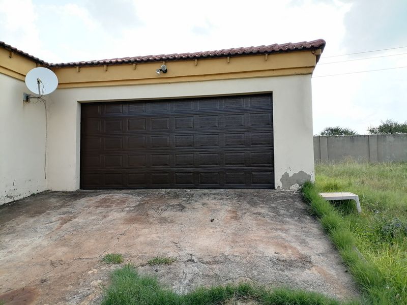 Exterior view of a single garage featuring a dark brown sectional door, tiled roof, and a concrete driveway requiring maintenance.