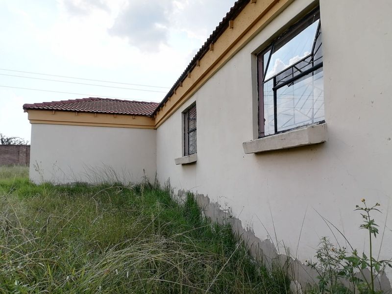 Rear exterior view of the property showing plastered walls with peeling paint, steel windows with security bars, and a tiled roof.