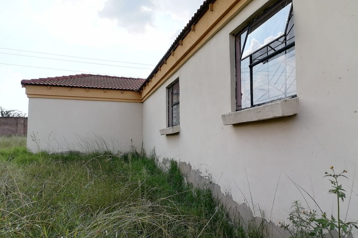 Rear exterior view of the property showing plastered walls with peeling paint, steel windows with security bars, and a tiled roof.