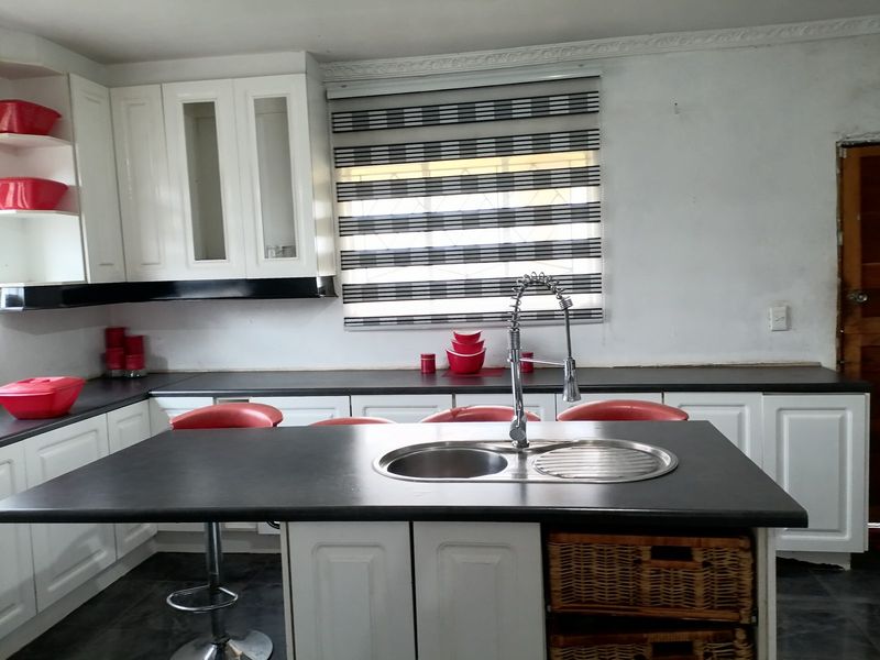A functional kitchen featuring white cabinetry, a central island with a double sink, and dark countertops, offering a clean and practical workspace.