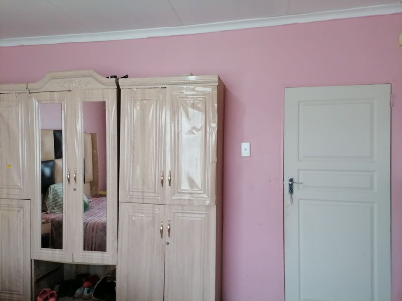 A bedroom interior featuring pink walls, a built-in cupboard unit, and a standard panel door.