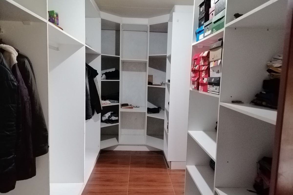 A walk-in closet featuring extensive white built-in shelving and cabinetry with tiled flooring.