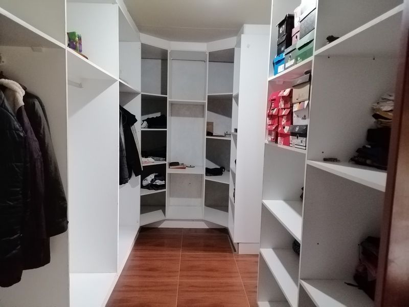 A walk-in closet featuring extensive white built-in shelving and cabinetry with tiled flooring.
