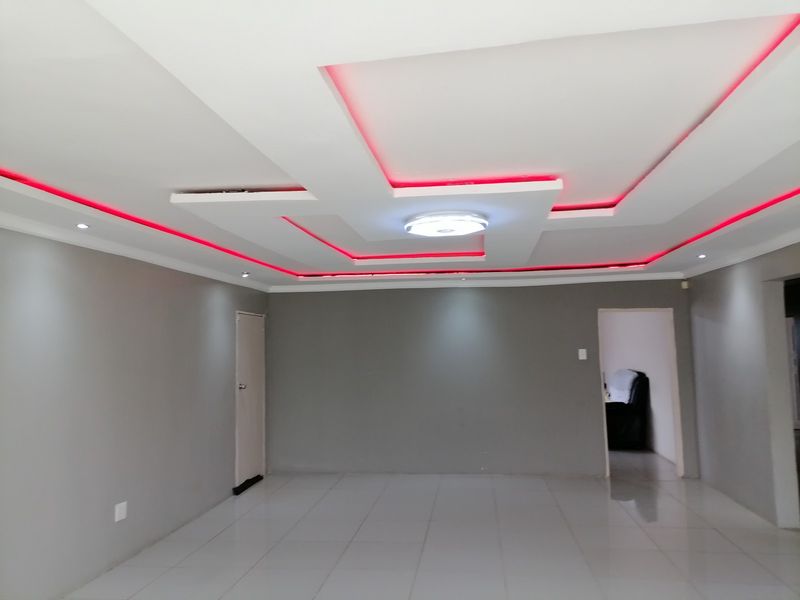 Spacious living area featuring a modern recessed ceiling design with integrated red LED accent lighting and neutral tiled flooring.