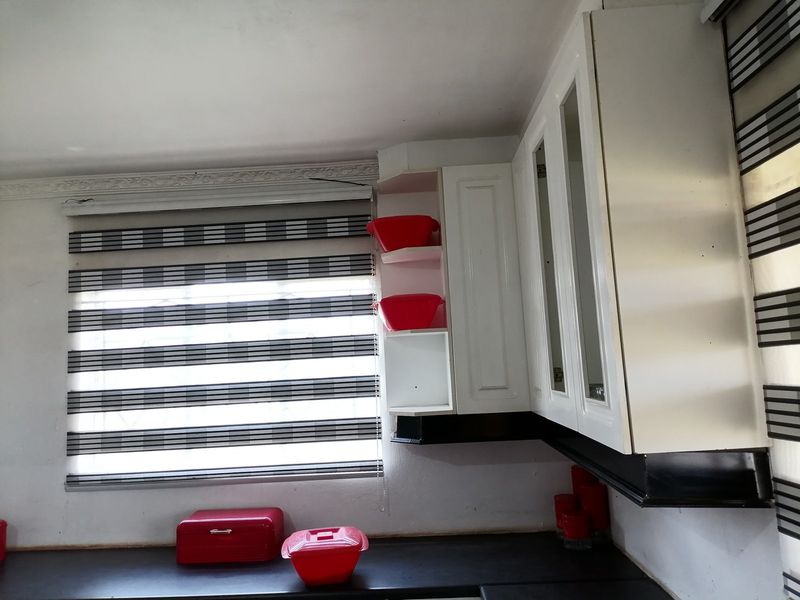 A well-maintained kitchen area featuring white built-in cabinetry, dark countertops, and modern window blinds.